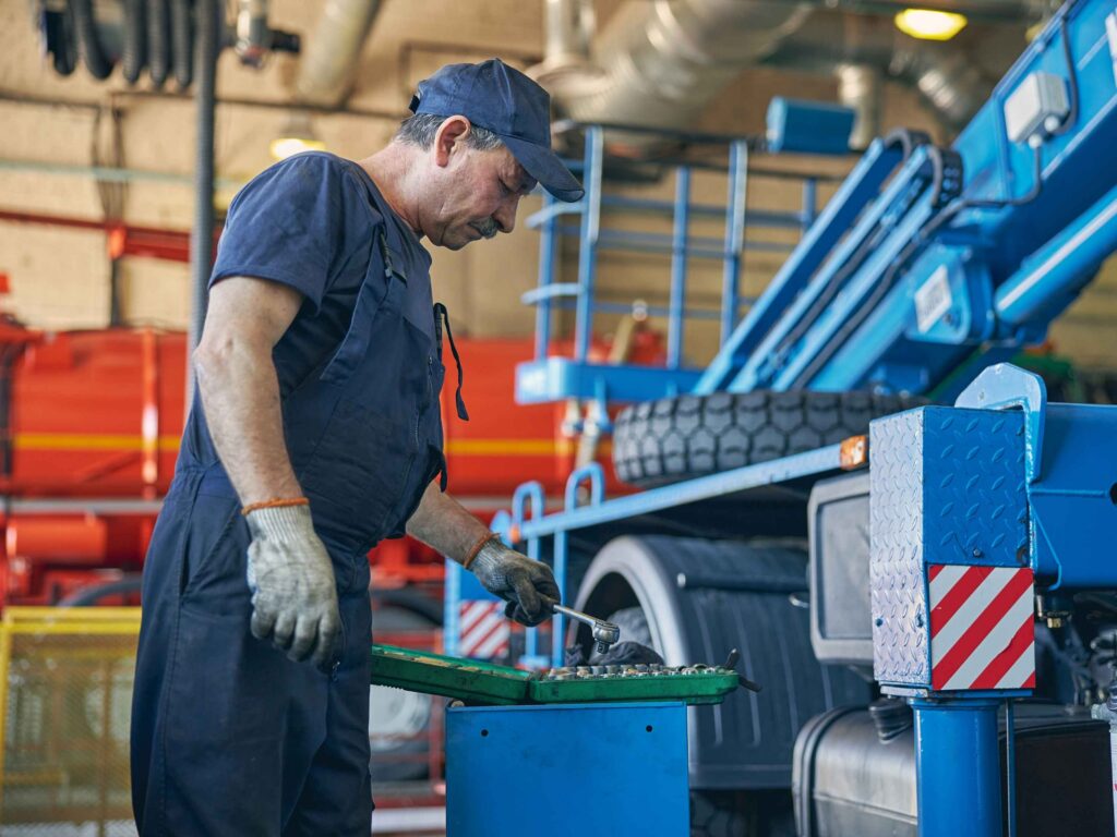 GO (19) Mechanic Repairing Blue Crane Truck in Garage