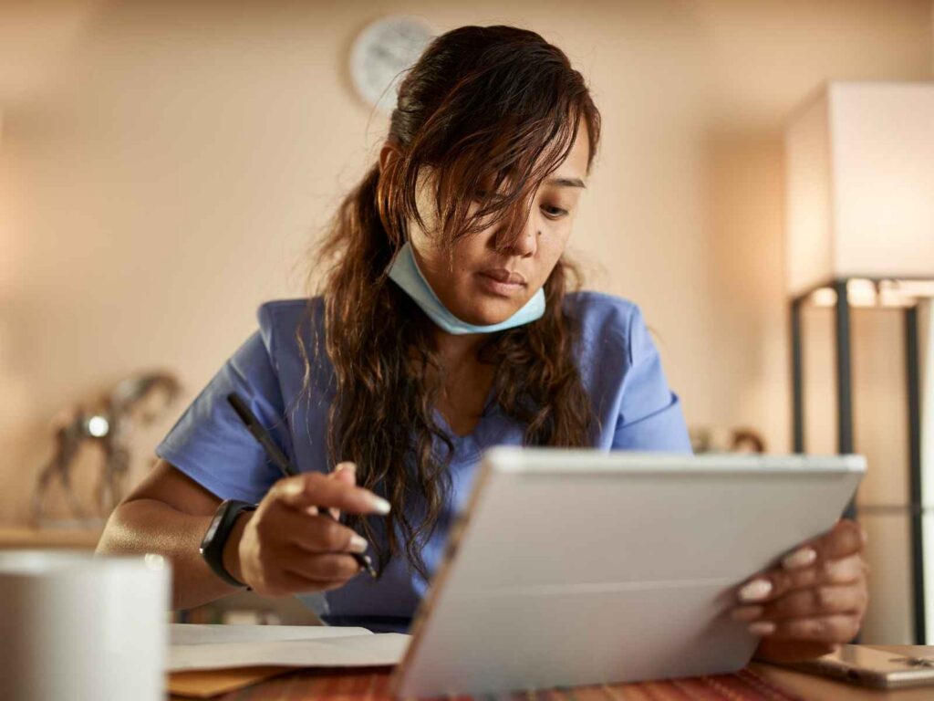 Woman in Scrubs Working on a Tablet at Home