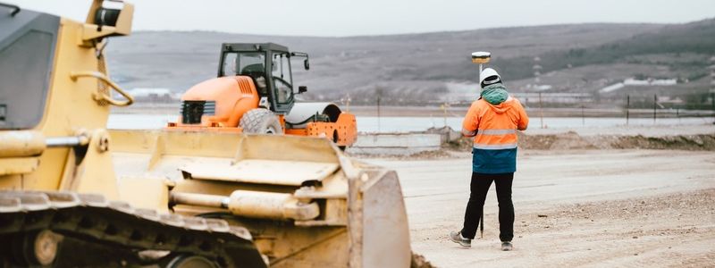 Heading (16) Construction Worker Inspects Site with Heavy Equipment